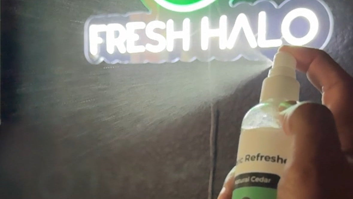 Person holding a spray bottle labeled 'Fresh Halo' in front of a neon sign.